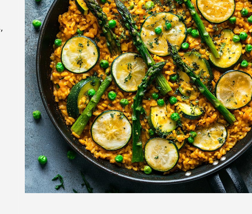 Paella with asparagus, sugar snap peas, zucchini, and lemon wedges in a wide pan
